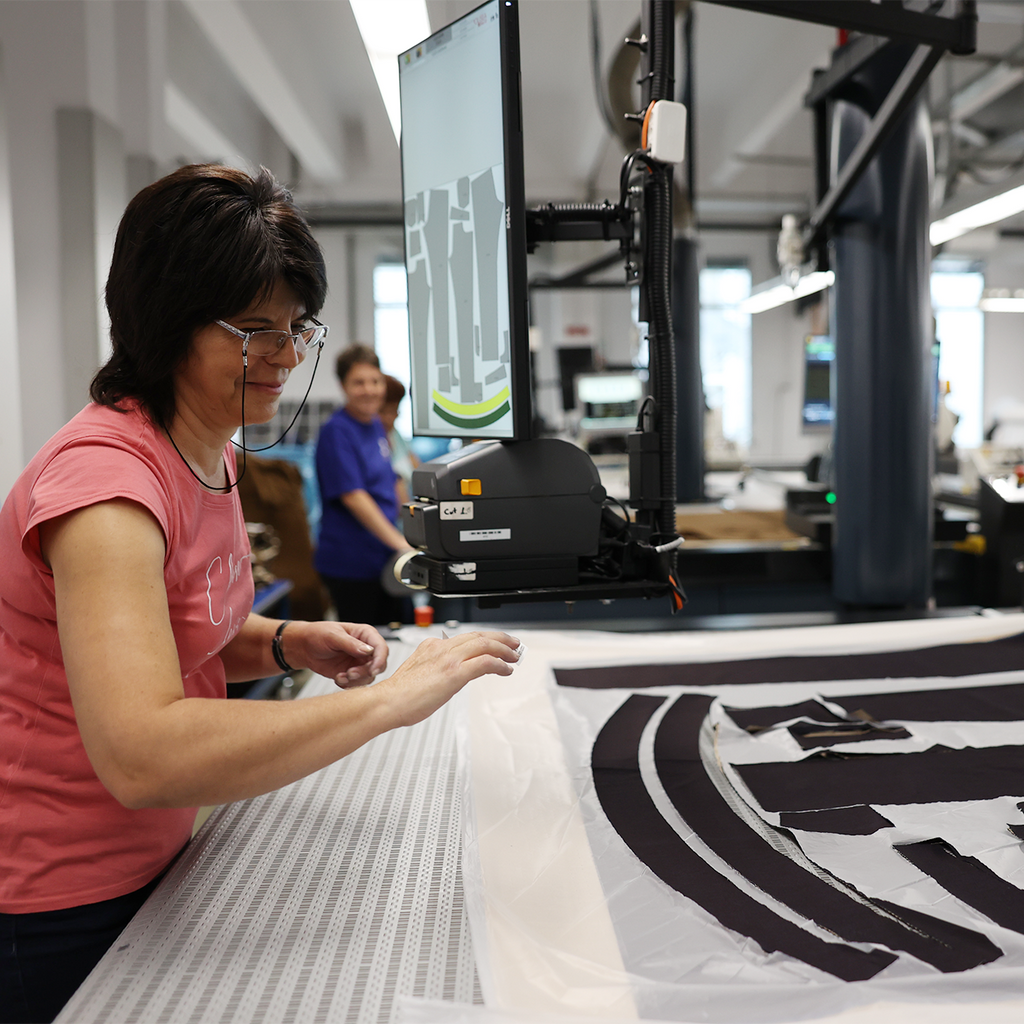 Person working with fabric and a large screen printer in a factory setting